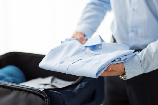 business, trip, luggage and people concept - close up of businessman packing clothes into travel bag