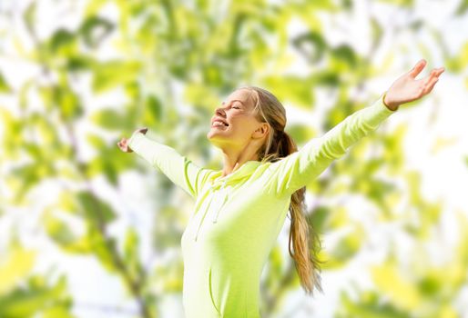 fitness, sport, happiness and people concept - happy woman raising hands over green tree leaves background