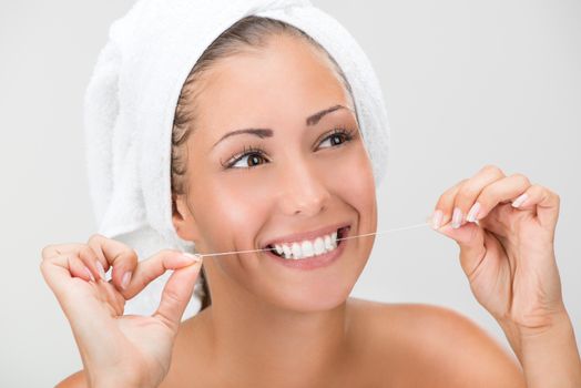 Cute girl preparing to start her day. She is cleaning teeth with dental floss. Looking at camera and smiling.