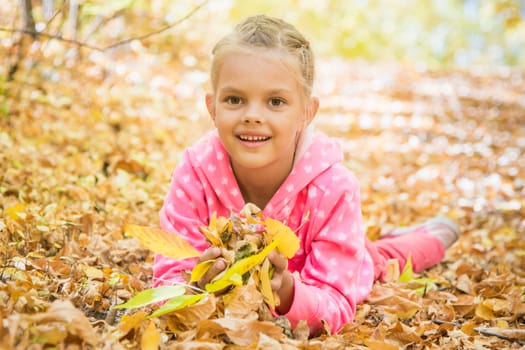 Six year old girl lying on the yellow fallen leaves in warm autumn day in the woods