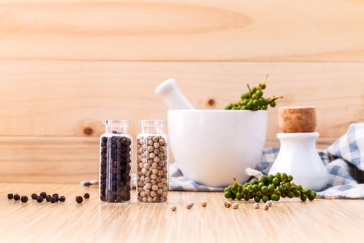 Assorted of spice bottles condiment black pepper ,white pepper and  green pepper seeds with mortar on wooden background.