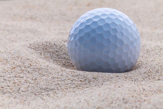 Close up golf ball in sand bunker shallow depth of field.