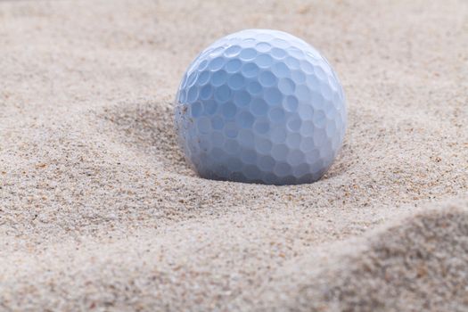 Close up golf ball in sand bunker shallow depth of field.