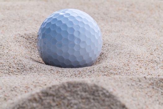 Close up golf ball in sand bunker shallow depth of field.