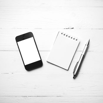 cellphone with notepad and pen over white table black and white color style