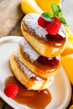 A stack of tree delicious german doughnuts powdered with sugar decorated with raspberry and raspberry sauce on white plate and yellow napkin