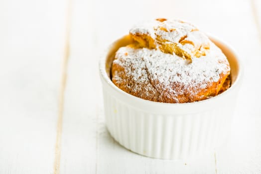 Small cakes with apple powdered with sugar in a ramekin on white wood table