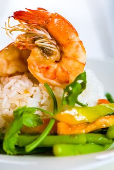 Dish with shrimps rice and green asparagus in a white plate, white background and white wood table