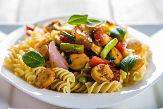 White pasta plate with vegetables and sausage on white background