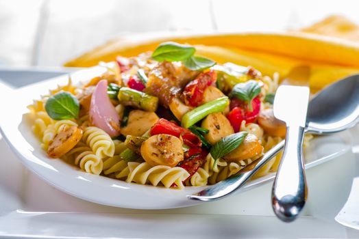 White pasta plate with vegetables and sausage on white background