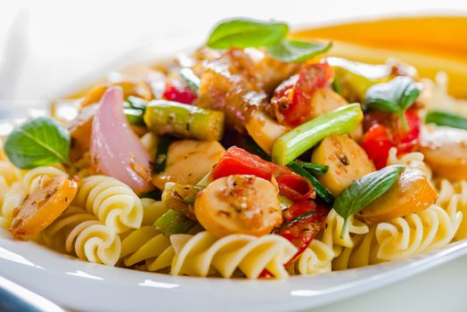 White pasta plate with vegetables and sausage on white background