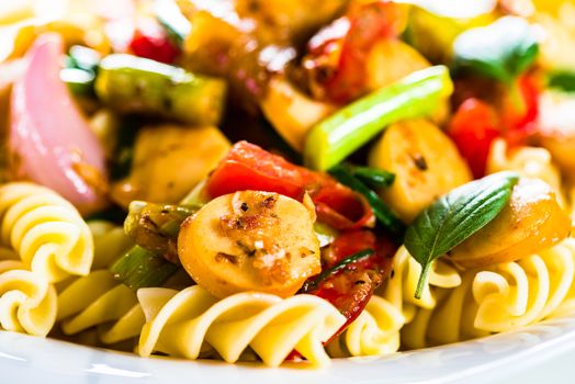 White pasta plate with vegetables and sausage on white background