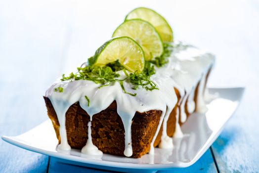 lemon loaf cake with icing decorating with lemon on white plate and blue wood table