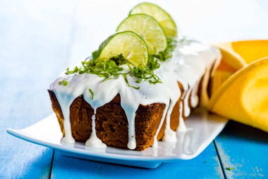 lemon loaf cake with icing decorating with lemon on white plate and blue wood table