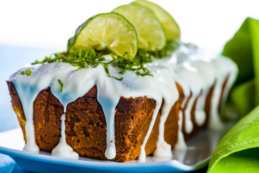 lemon loaf cake with icing decorating with lemon on white plate and blue wood table