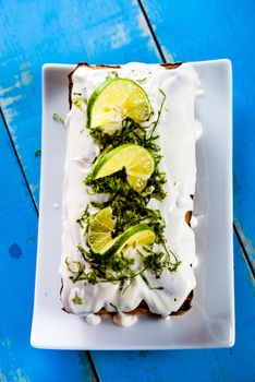 Top view of an lemon loaf cake with icing decorating with lemon on white plate and blue wood table