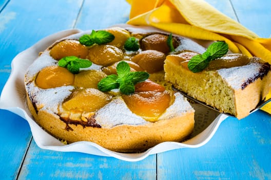 Homemade fresh apricot cake on blue wood table with yellow napkin