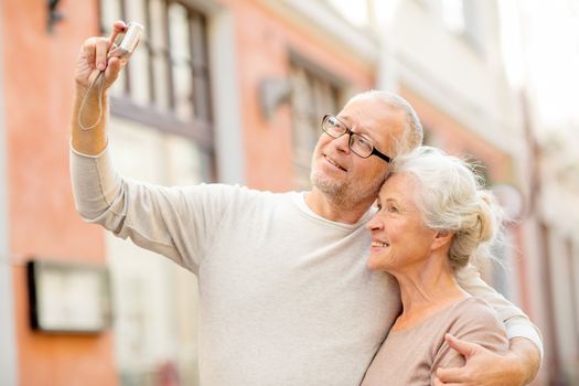 age, tourism, travel, technology and people concept - senior couple with camera taking selfie on street