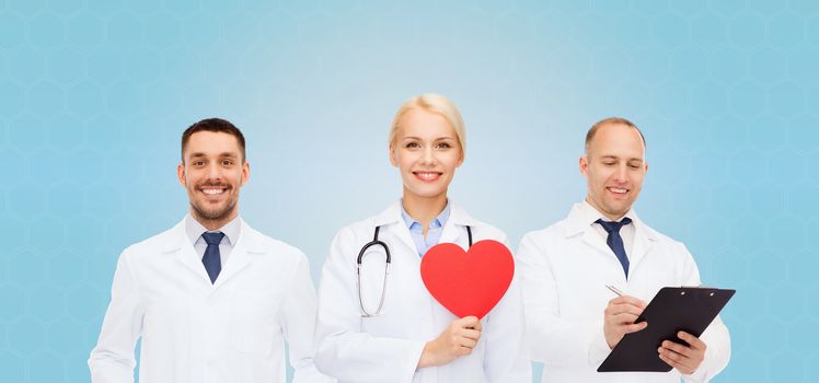medicine, profession, teamwork and healthcare concept - group of smiling medics or doctors holding red paper heart shape, clipboard and stethoscopes over blue background