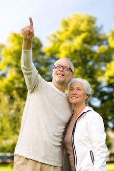 family, age, tourism, travel and people concept - senior couple hugging and pointing finger in park