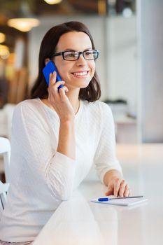 business, people, technology and lifestyle concept - smiling young woman in eyeglasses calling on smartphone at cafe