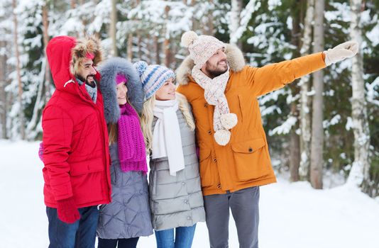 love, relationship, season, friendship and people concept - group of smiling men and women pointing finger in winter forest