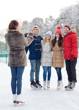 people, friendship, technology and leisure concept - happy friends taking picture with smartphone on ice skating rink outdoors