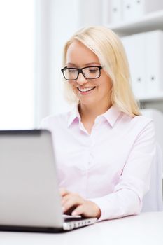 education, business and technology concept - smiling businesswoman or student in eyeglasses with laptop computer in office
