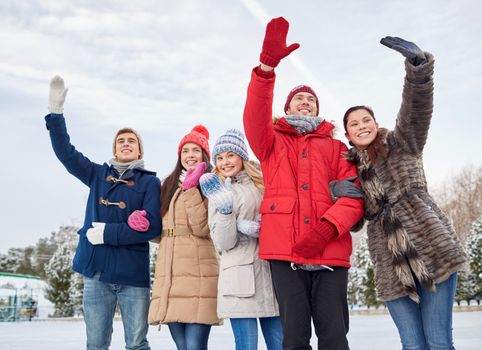 people, winter, friendship, sport and leisure concept - happy friends waving hands on ice rink outdoors