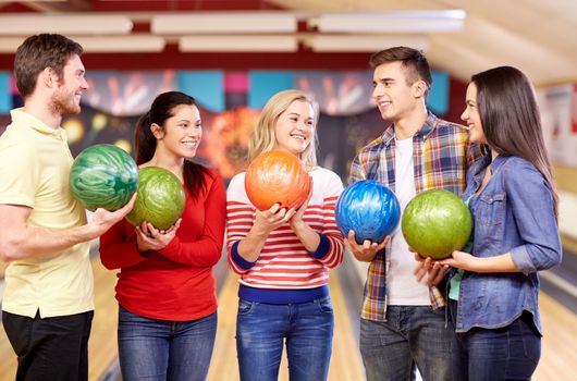 people, leisure, sport, friendship and entertainment concept - happy friends holding balls and talking in bowling club