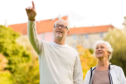 family, age, tourism, travel and people concept - senior couple pointing finger in city park