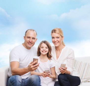 family, technology and people concept - smiling mother, father and little girl with smartphones over blue sky background