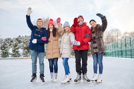 people, winter, friendship, sport and leisure concept - happy friends ice skating and waving hands on rink outdoors