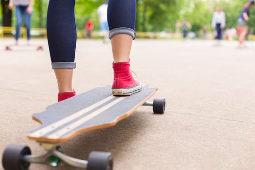Teenage girl wearing blue jeans and sneakers practicing long board riding in skateboarding park. Active urban life. Urban subculture.