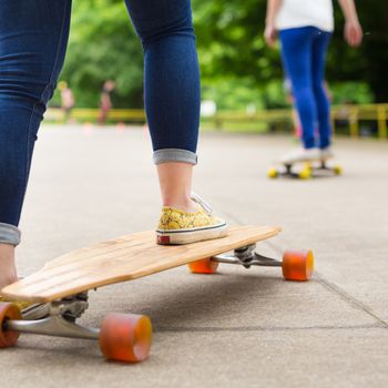 Teenage girl wearing blue jeans and sneakers practicing long board riding in skateboarding park. Active urban life. Urban subculture.