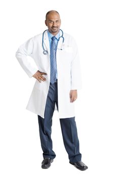 Full length mature Indian male medical doctor in uniform standing isolated on white background.