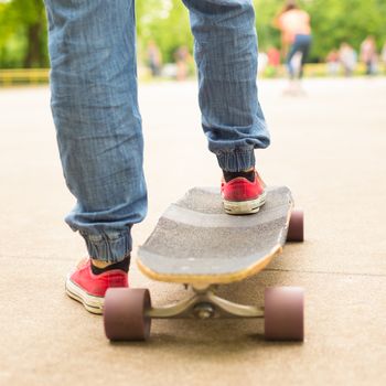 Teenage girl wearing blue jeans and sneakers practicing long board riding in skateboarding park. Active urban life. Urban subculture.