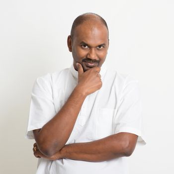 Portrait of mature casual business Indian man looking at camera and smiling, copy space on side, standing on plain background with shadow.