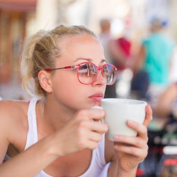 Calm casual blond lady enjoying cup of coffee outdoor in typical italian  street coffee house on warm summer day.