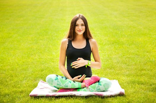 The beautiful pregnant woman practices yoga on a lawn