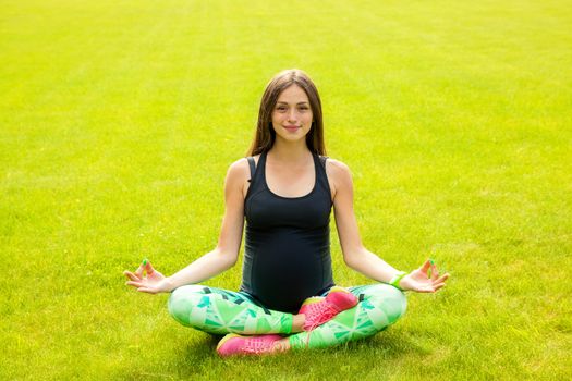 The beautiful pregnant woman practices yoga on a lawn