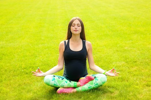 The beautiful pregnant woman practices yoga on a lawn