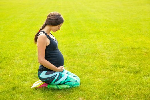 The beautiful pregnant woman practices yoga on a lawn