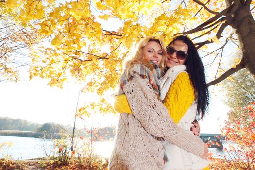 Two pretty young women hug in autumn park