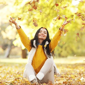 Woman drop up leaves siting in autumn park