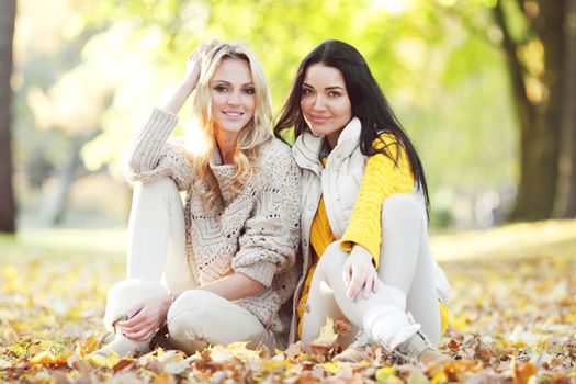 Happy female friends sitting on ground in autumn park