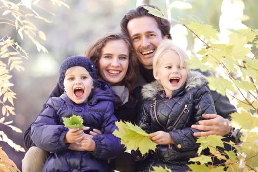 Portrait of a happy family in autumn park with maple leaves