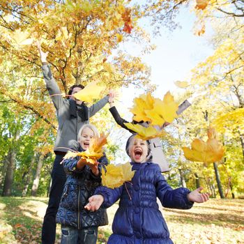 Happy family playing with autumn maple leaves in park