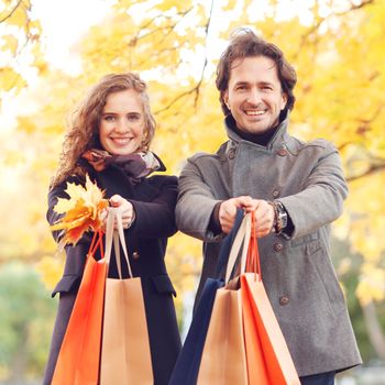 Happy smiling couple with shopping bags in autumn park