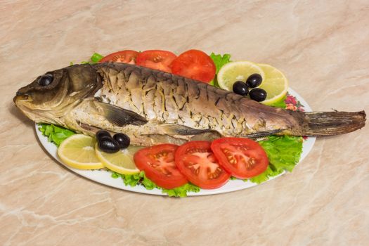 The photo shows a fish on a plate with tomatoes and olives.